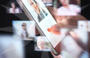 Close-up of a fingertip tapping a heart icon on a smartphone screen with floating photo thumbnails around.